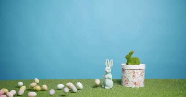 Rabbit Toy on a Blue Background of Green Grass with many colored eggs, Text. — Stock Video