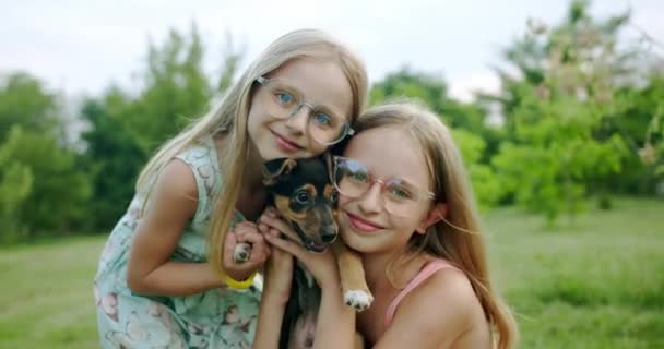 Zwei Mädchen umarmen und küssen einen kleinen Hund, spielen mit entzückenden Welpen im Freien — Stockvideo