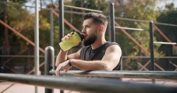 Спортсмен расслабляется и пьет воду из бутылки после интенсивной тренировки. — стоковое видео