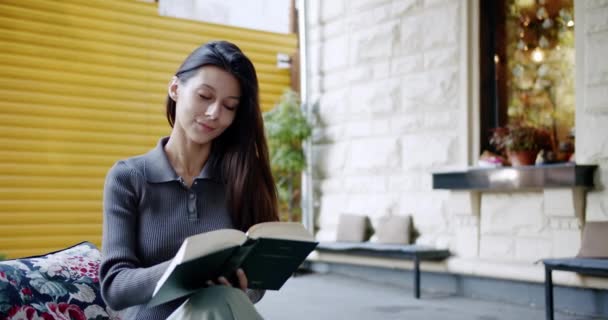 Lächelnde junge Frau liest im Freien interessantes Buch und blättert in einem Buch — Stockvideo