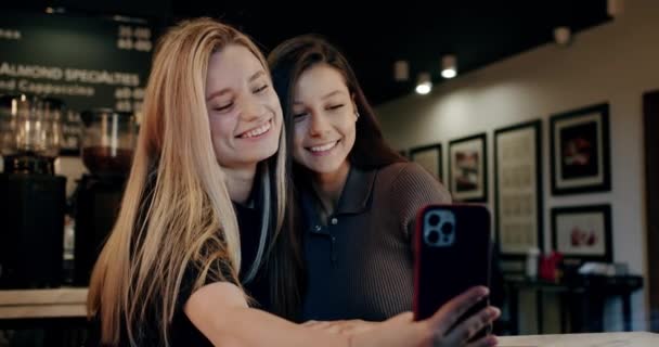 Dwie młode kobiety robiące sobie selfie w kawiarni. Odpoczywając rozmawiając używaj telefonu. — Wideo stockowe