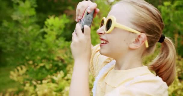 Chica adolescente en vestido amarillo, curioso fotografiado en la naturaleza con cámara retro — Vídeos de Stock