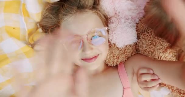 Una niñita feliz con gafas, descansa y envía saludos con su mano — Vídeos de Stock