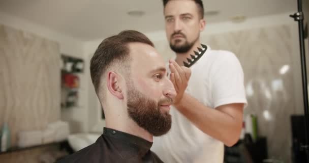 Fryzjer ustawia włosy przez spray i grzebie je. Nowoczesna fryzura w salonie fryzjerskim. — Wideo stockowe