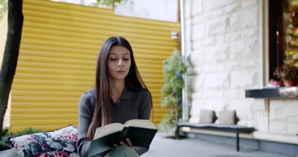 Lächelnde junge Frau liest im Freien interessantes Buch und blättert in einem Buch — Stockvideo