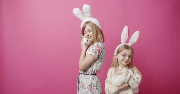 Симпатичные девочки с кроличьими ушами, играющие с кроликом на изолированном фоне — стоковое видео