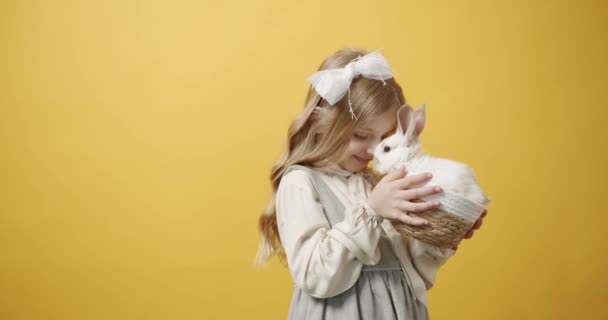 Niña sonríe en un vestido blanco sostiene una canasta con un conejo en sus manos — Vídeos de Stock