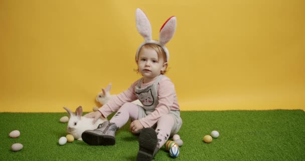 Ein 2-jähriges Kind spielt mit Kaninchen auf einem grünen Teppich mit bunten Eiern — Stockvideo