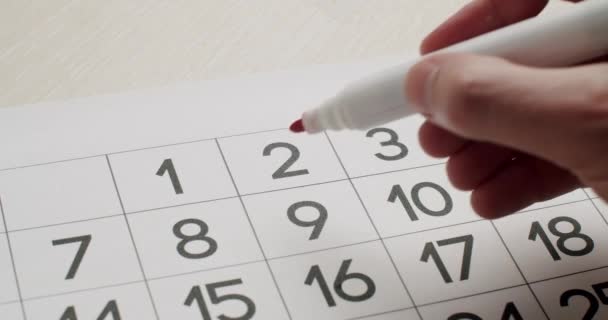 Mans hand Notez le 2ème jour sur le calendrier en papier à l'aide d'un stylo rouge. — Video