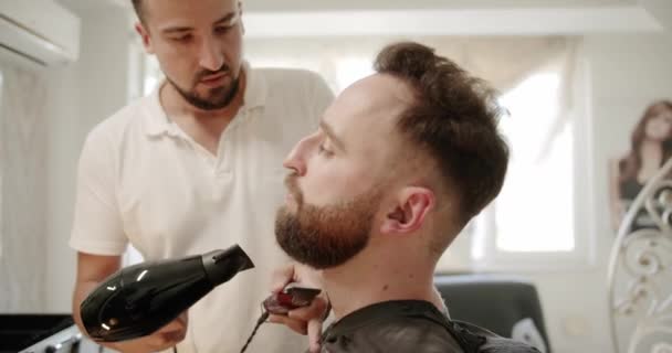 美容師はヘアドライヤーで動作し、ひげを結びます。美容師. — ストック動画