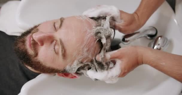 Ο άντρας στο σαλόνι ομορφιάς σερβίρεται, πλένει το κεφάλι του με σαμπουάν και νερό. — Αρχείο Βίντεο