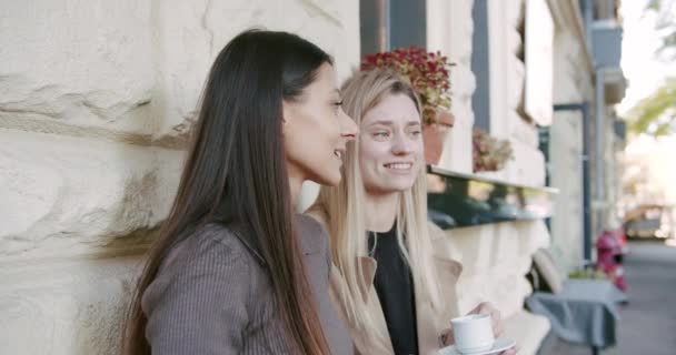 Дві дівчини відпочивають, подають каву і чай, розмовляють і посміхаються біля тераси — стокове відео