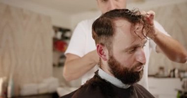 Makasla saç kesen bir erkek, yakın plan. Bir stilistin hizmetleri alınıyor.