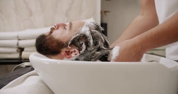 Мужчина в салоне красоты подается, омывая голову шампунем и водой — стоковое видео