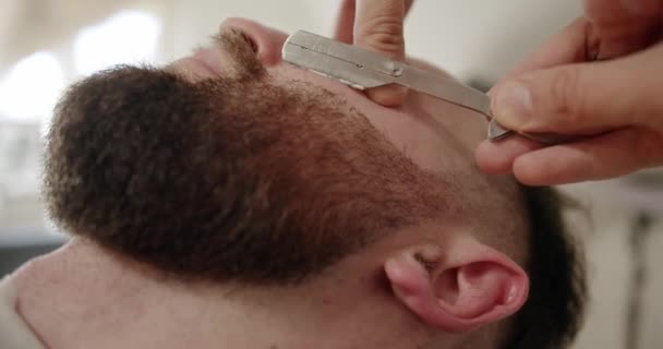 Профессиональный парикмахер бреет бороду клиента бритвой. Бородатый порез — стоковое видео