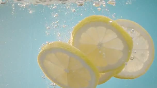 Lambat Gerak jatuh Lemon irisan ke dalam percikan air di latar belakang biru — Stok Video