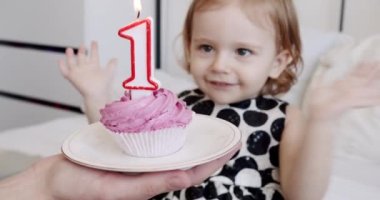 1 yaşında mutlu bir kızın doğum günü partisi ve pastaya mum üflemesi..