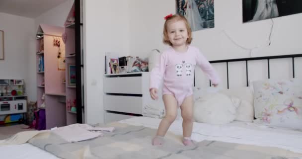 La niña de 1 año juega en casa, salta de alegría y sonríe maravillosamente. — Vídeo de stock