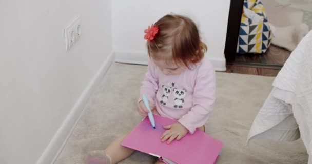 Το κοριτσάκι παίζει στο παιδικό δωμάτιο και ζωγραφίζει σε ένα σημειωματάριο.. — Αρχείο Βίντεο