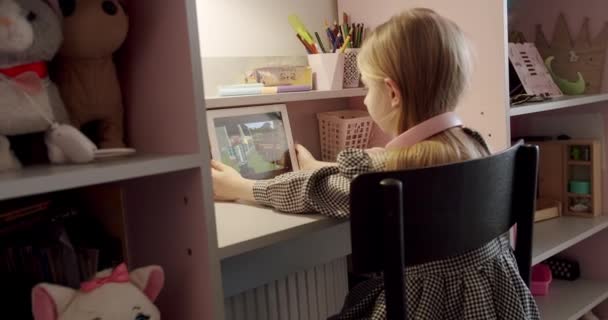 Niña en la habitación de los niños con auriculares rosados usando tableta digital — Vídeo de stock