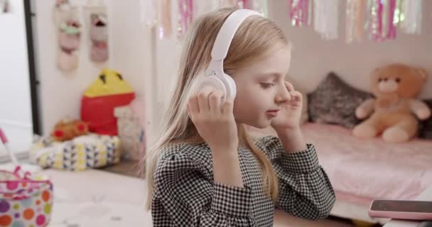 Het 7-jarige meisje in de kinderkamer met koptelefoon en smartphone. — Stockvideo