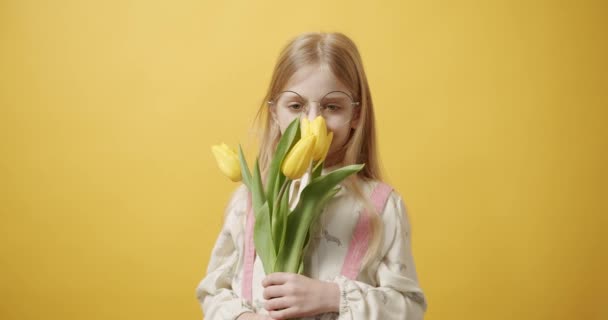 Hermosa chica sostiene flores de tulipán en su mano sonríe sobre fondo amarillo — Vídeo de stock