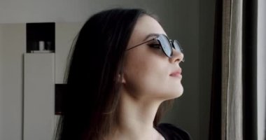 Modern evde güneş gözlüklü, koyu renk saçlı, güzel bir kadının portresi.