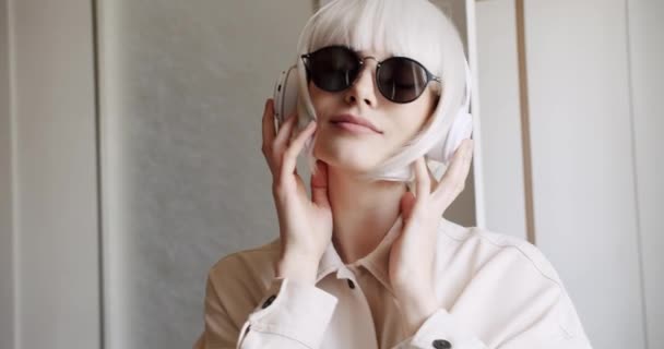 Lächelnde junge Hipsterin hört Musik in weißen, drahtlosen Kopfhörern. — Stockvideo