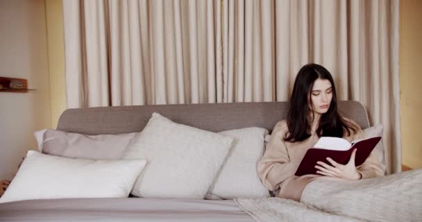 女性は家でベッドの上で本を読んでいる。リラックスして教育の概念のための時間 — ストック動画