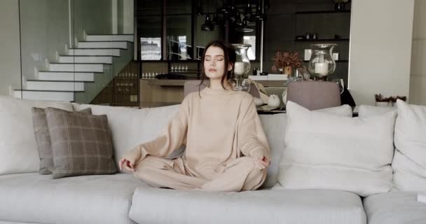 Fiatal nyugodt nő pihentető lótuszpozícióban és csukott szemmel kényelmes kanapén — Stock videók