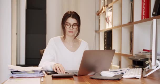 Mulher bonita em óculos Funciona no computador portátil enquanto no escritório. — Vídeo de Stock