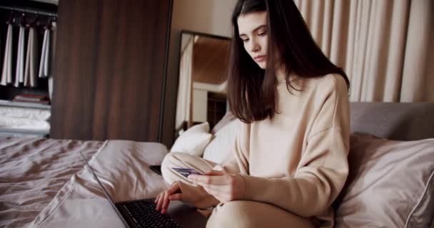 Mujer joven sosteniendo tarjeta de crédito haciendo pago en línea en el ordenador portátil en el hogar moderno — Vídeo de stock