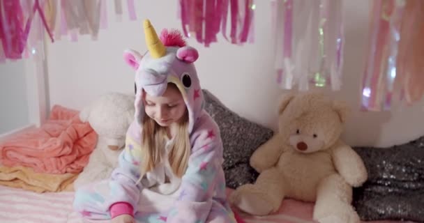Очаровательная маленькая 7-летняя девочка, играющая в костюме единорога со многими игрушками — стоковое видео