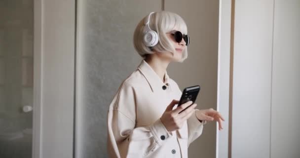Hermosa mujer con cabello blanco usando teléfono móvil con auriculares inalámbricos — Vídeos de Stock