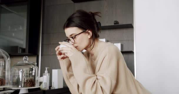 Μια όμορφη νεαρή γυναίκα πίνει τσάι στο μοντέρνο δωμάτιο κουζίνας στο σπίτι, — Αρχείο Βίντεο
