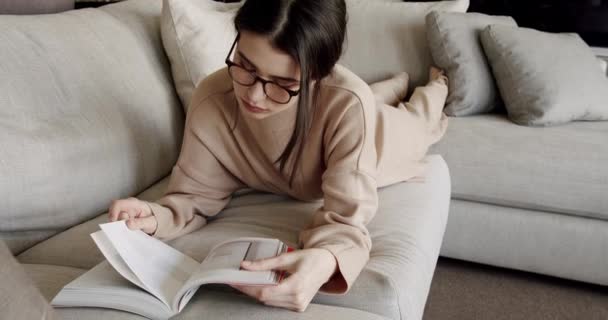 夢のような女性は屋内読書本に座って、現代の家で居心地の良い怠惰な週末をお楽しみください — ストック動画