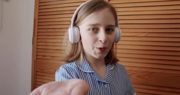 Teenage dívka tanec a úsměv s bezdrátovými sluchátky a dát virtuální polibek — Stock video