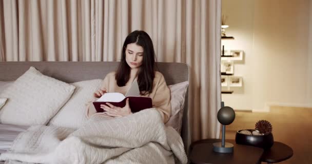 Mulher relaxando na cama e lendo um livro no quarto na casa moderna — Vídeo de Stock