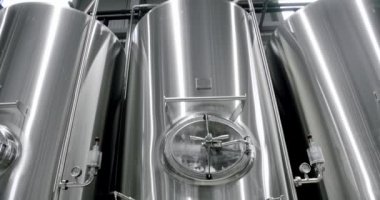 Panning shot of rows of large steel tanks with beer in industrial brewery plant.