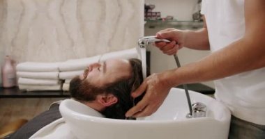Güzellik salonunda çekici bir adama berber servis ediyor, kafasını şampuan ve suyla yıkıyor profesyonel lavaboda lüks bir güzellik salonunda. Güzellik Salonunda servis