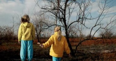 The younger sisters dressed in the colors of the Ukrainian flag embrace and encourage each other on a background of earth burned during the war. Stop the war in Ukraine. homeless child. No War.