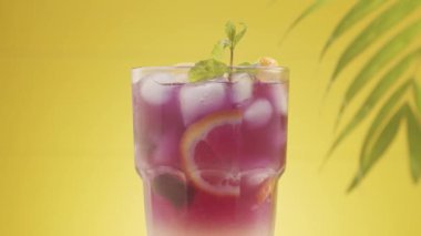 Buzlu, limonlu ve naneli ferahlatıcı yaz limonata kokteyli, yaz ferahlatıcı kokteyl, sarı arka planda deniz kumu ve tropikal yapraklarla çekilmiş bir stüdyo çekimi. Limonlu Kokteyl.