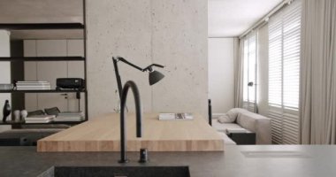 Minimalist bir dairede modern mutfak odası. Yemek alanı doğal ahşap. Kara Mutfak lavabosu ve musluğu var. Evin içi beyaz, gri renkler, beton ve konforlu ekipmanlar..