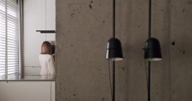 Modern bir mutfak odasında, minimalist bir dairede, beyaz bir evde, beton ve konforlu donanımlı gri renkli bir evde bir kadın kahve yapıyor. modern tasarım ve dekorasyona sahip ev aletleri.