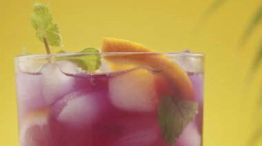 Yaz ferahlatıcı kokteyl, sarı arkaplanda deniz kumu ve tropikal yapraklarla çekilen stüdyo çekimi. Citrus Kireç Kokteyli. Buzlu, limonlu ve naneli ferahlatıcı yaz limonata kokteyli..