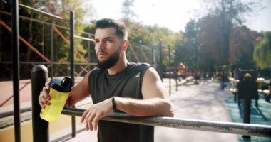 Atletik adam yorucu bir kardiyodan sonra su içiyor. Isınma turundan sonra genç ve hevesli vücut geliştirici. Spor ve spor teknolojisi konsepti spor salonu konsepti. Sağlıklı yaşam tarzı ve açık hava eğitimi