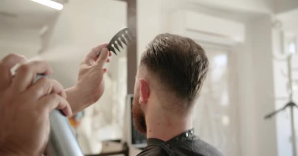 魅力的な男性は理容室の店で現代的な散髪を得ています バーバーはスプレーで髪を設定し それらを結合します バーバーショップ 美容師はレトロなヘアサロンで散髪をしています メンズヘアスタイリング — ストック動画