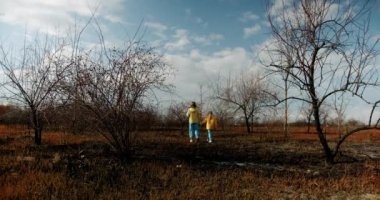 The younger sisters dressed in the colors of the Ukrainian flag embrace and encourage each other on a background of earth burned during the war. Stop the war in Ukraine. homeless child. No War.