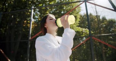 Yorucu bir kardiyodan sonra su içen atletik bir kadın. Genç vücut geliştirici kız ısındıktan sonra dinleniyor. Spor ve spor teknolojisi konsepti spor salonu konsepti. Sağlıklı yaşam tarzı ve açık hava eğitimi