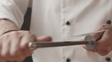 Şef 'in et kesmeden ya da yemek yapmadan önce serin bir bıçak keskinleştirdiği yakın çekim. Profesyonel aşçı iş için bir enstrüman hazırlıyor. Aşçı, evcil mutfakta bıçağını biler..